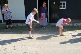 Twee kinderen met ouderwetse hoepel, op achtergrond meisje in klederdracht